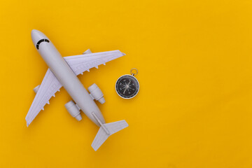 Minimalism travel, adventure flat lay. Compass and air plane on yellow background. Copy space. Top view
