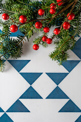 Christmas border with firtree, holly and Christmas wreath and red berries on blue and white geometric background,