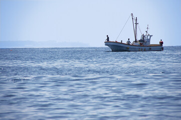 岬の沖で釣り糸を垂らす釣り船