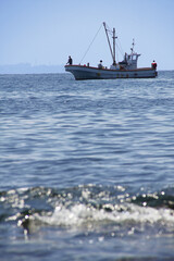 岬の沖で釣り糸を垂らす釣り船と浅瀬の波