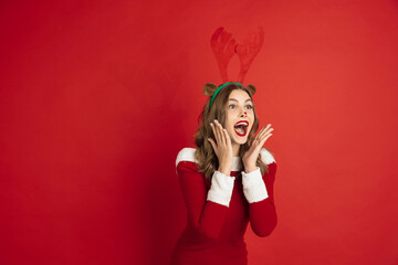 Shocked. Greetingcard. Concept of Christmas, 2021 New Year's, winter mood, holidays. Copyspace for ad, postcard. Beautiful caucasian woman with long hair like Santa's Reindeer catching giftbox.