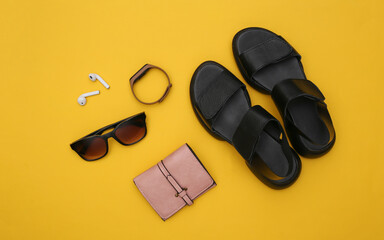 Gadgets and women's accessories on a yellow background. Sandals, smart bracelet, headphones, sunglasses and wallet. Top view. Flat lay