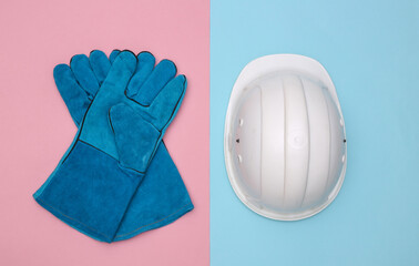 Work gloves and construction safety helmet on pink blue background. Top view
