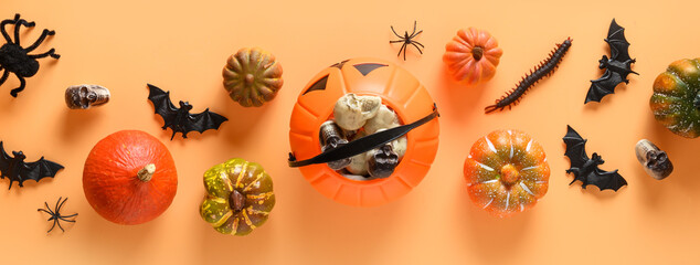 Halloween banner of fun party decorations, candy bowl, pumpkins, sweets, bat, skulls, spooky spider on orange background. View from above, flat lay.