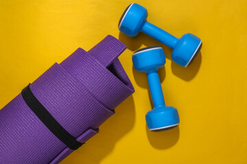 Rolled fitness mat, dumbbells on a bright yellow background. Healthy lifestyle, sport concept. Top view Flat lay