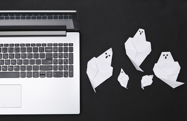 Laptop and origami ghosts on black background. Halloween theme. Top view