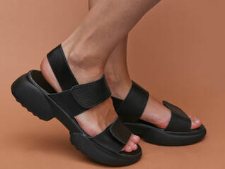 Female feet in fashionable leather sandals on brown background