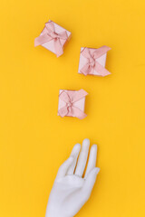 White mannequin hand and gift boxes on yellow background. Top view