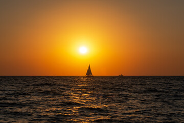 A lone sailboat at sunset. Atmospheric seascape with orange sun. Cloudless sky. The concept of relaxation and relaxation. Idyll. Sea with a little excitement. Sailboat out of focus.