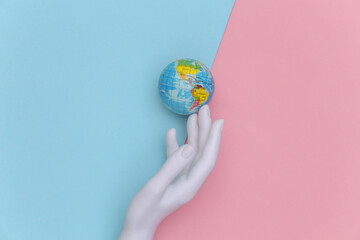 The mannequin's white hand touches globe on pink blue background. Save planet. Top view