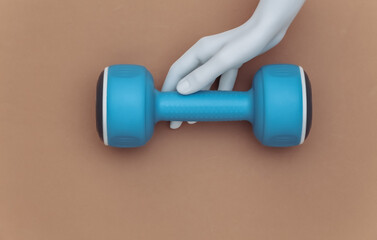 White mannequin hand holds plastic dumbbells on brown background. Sport and fitness concept