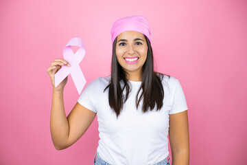 Young beautiful woman wearing pink headscarf holding brest cancer ribbon over isolated pink background with a happy face standing and smiling with a confident smile showing teeth