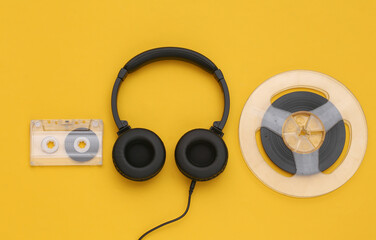 Stereo headphones and magnetic audio reel, audio cassette on yellow background. Top view. Flat lay
