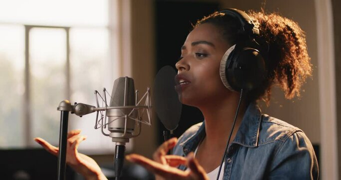 Music production. Portrait of african american lady singer recording song, singing in headphones to mic at sound record studio