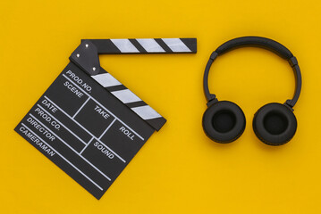 Movie clapperboard and stereo headphones on a yellow background. Top view