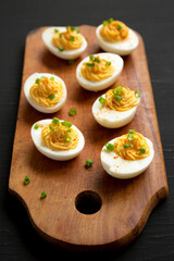 Homemade Deviled Eggs with Chives on a rustic wooden board on a black background, low angle view....