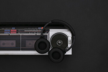Boombox audio tape recorder and stereo headphones on black background. Retro 80s. Top view. Flat lay