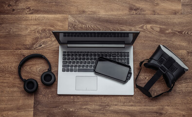 Flat lay composition of modern gadgets. Laptop, vr helmet, headphones, smartphone on wooden...