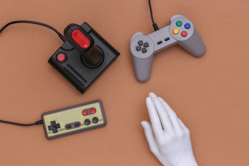 Mannequin hand touching retro joysticks on brown background. Top view, minimalism
