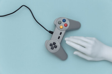 Mannequin hand touching retro gamepad on blue background. Top view. Creative art, minimalism