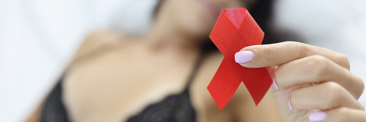 Woman is holding red ribbon while lying on t bed. HIV prevention and health safety concept