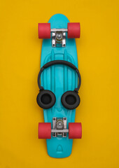 Flat lay composition of youth hipster accessories. Cruiser board and headphones on yellow background. Top view
