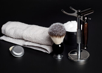 Razor and brush on stand, towels, perfume, balsam and blades on a black background.