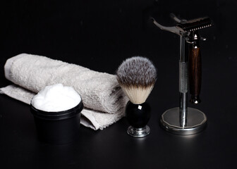 Razor and brush on stand, towels, perfume, balsam and blades on a black background.