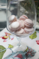 Fototapeta na wymiar rose gold dusty pink filled macaroons served in a large glass vase on a white table with a floral table cloth