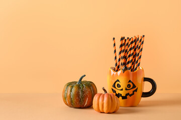Halloween fun party decorations, pumpkins, mug with drinking straw on orange background. Horizontal...