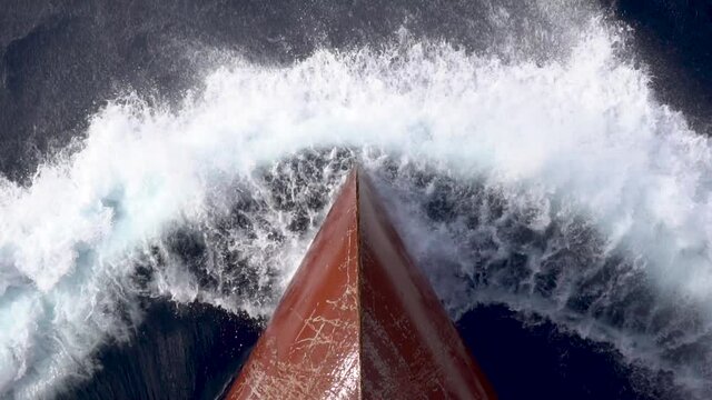 Top view of red metal bow of the vessel cutting sea surface with foamy splashes.
