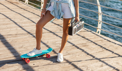 Young woman with skeetboard and retro tape recorder on the beach on a bright sunny day