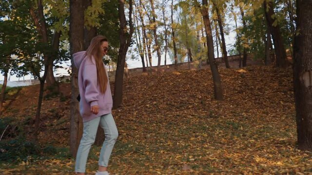 Side view of Beautiful happy smiling young woman wearing pink hoodie walking in autumn park. Season and people concept. Nature, slow motion.