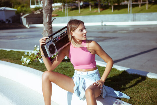 80s style image of young attractive woman with boombox audio tape recorder on bright sunny day outdoors