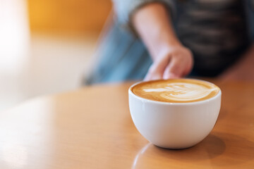 Closeup image of a hand holding a white cup of coffee on wooden table