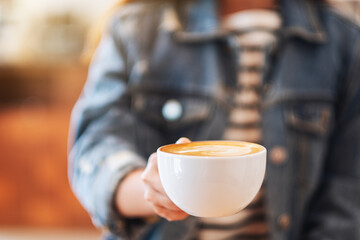Closeup image of a woman holding and showing a cup of coffee in cafe