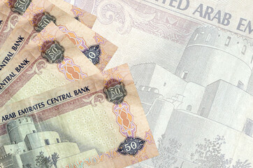 50 UAE dirhams bills lies in stack on background of big semi-transparent banknote. Abstract...