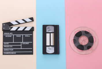 Movie clapper board, video cassette and film reel on colored pastel background. Cinema industry,...