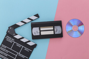 Film clapper board and cd's, video cassette on pink blue background. Cinema industry, entertainment. Top view