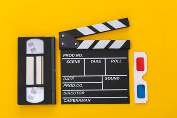 Film clapper board, 3d glasses, video cassette on yellow background. Top view