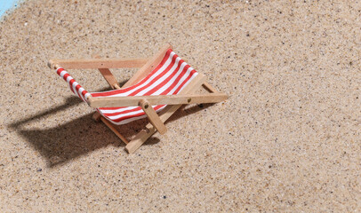 Fototapeta na wymiar Summer beach travel vacation concept. Mini beach deck chair on sand at bright sunny day.