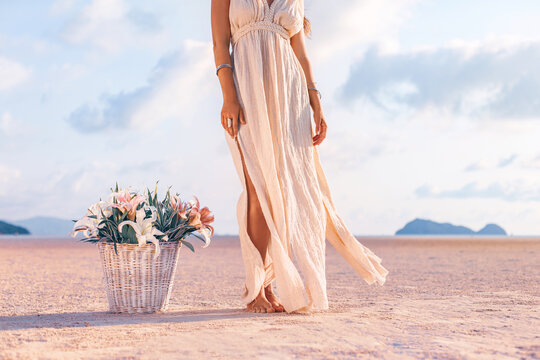 beautiful young stylish woman with basket with flowers on sand at sunset