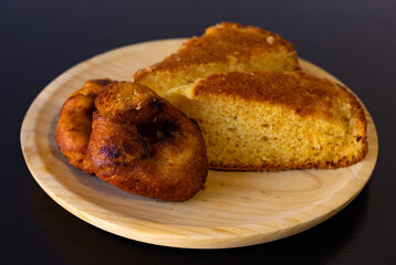 View from a top angle of a few pieces of sponge cake and rustic homemade doughnuts on a wooden plate with a black background