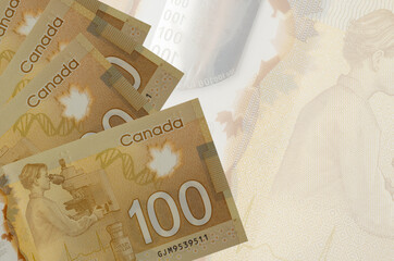 100 Canadian dollars bills lies in stack on background of big semi-transparent banknote. Abstract...