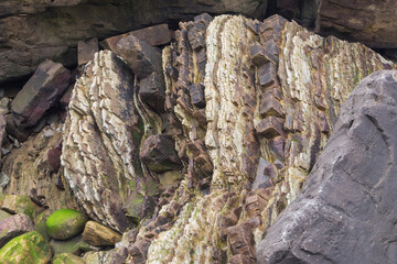 Flysch de material sedimentario en capas de roca de distintos colores, texturas y durezas en acantilado junto al mar - obrazy, fototapety, plakaty