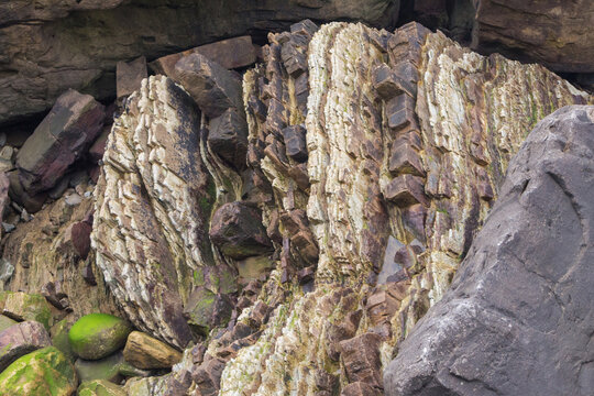 Flysch de material sedimentario en capas de roca de distintos colores, texturas y durezas en acantilado junto al mar