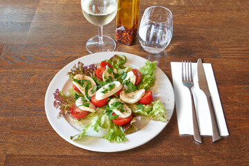 Silverware on Brown wooden table and white plate with tomatoes and mozzarella