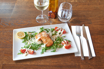 Silverware on Brown wooden table and plate with shrimp and cheese croquettes on tomato and salad.