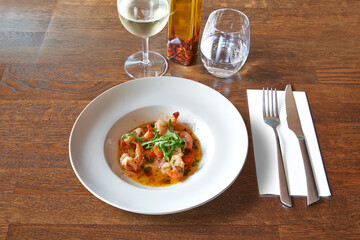Silverware on Brown wooden table with white round plate and garlic shrimps.