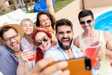 Group of young people having fun at summer vacation and enjoying a poolside party with drinks and making selfie.	